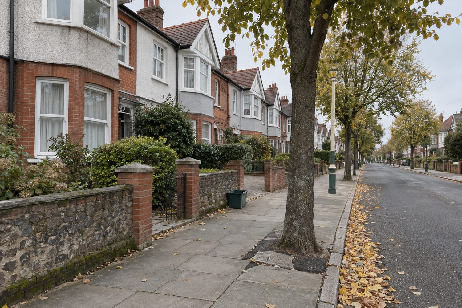 Two-storey terraced houses with bay windows and gables along a tree-lined pavement on an overcast autumn day