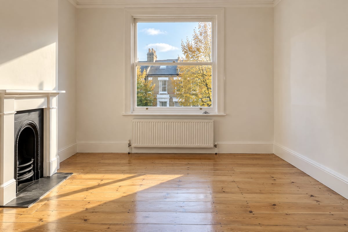 An empty room with bare pine floorboards, a fireplace, a radiator and a sash window, with a set of keys on the window board.
